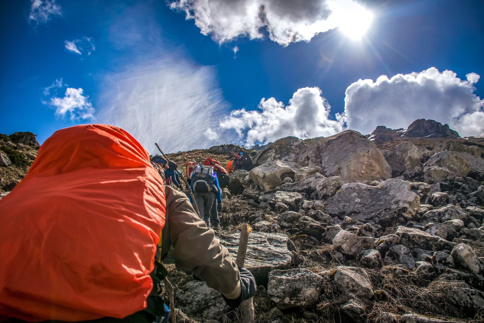 Hikers ascending a rocky mountain trail under a bright sunlit sky.
