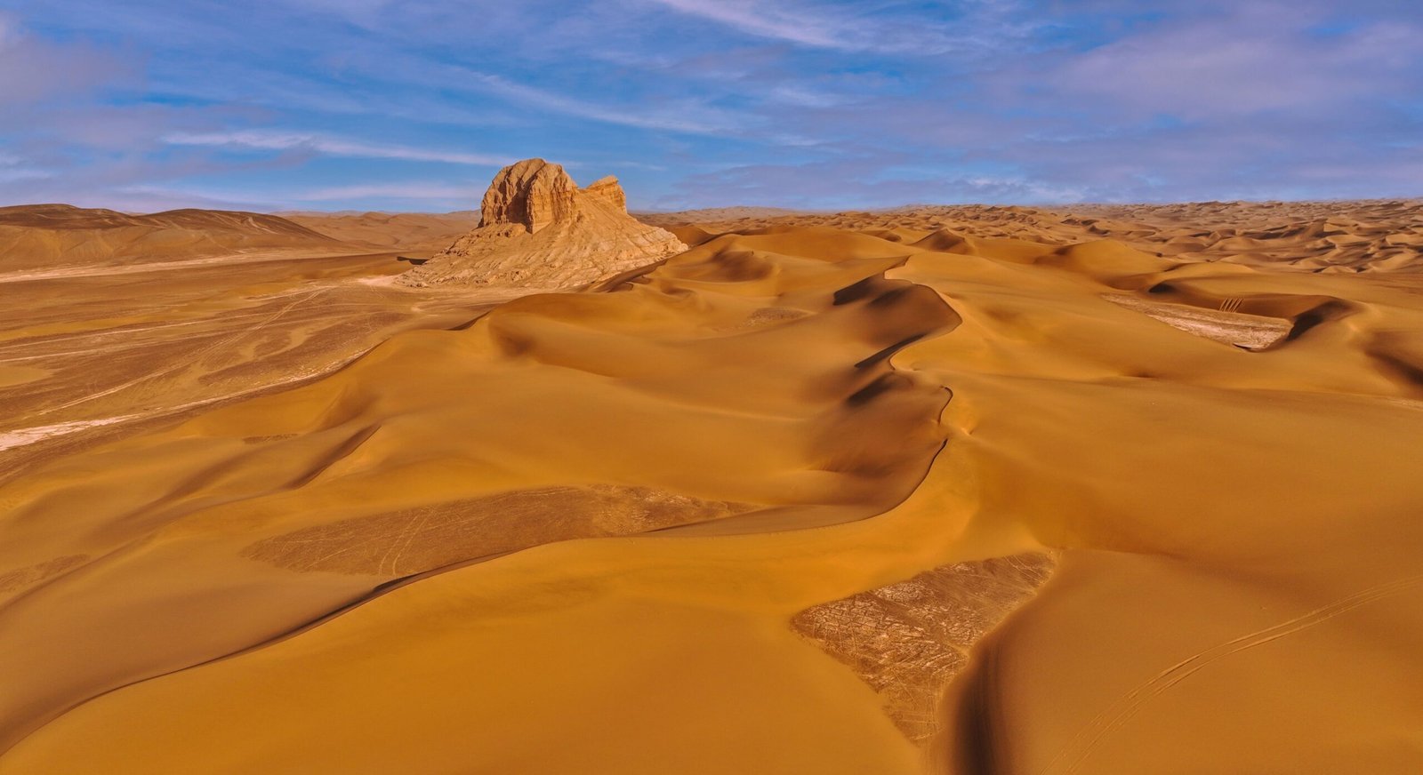 Sweeping view of golden desert dunes with a clear blue sky, showcasing the arid landscape's beauty.