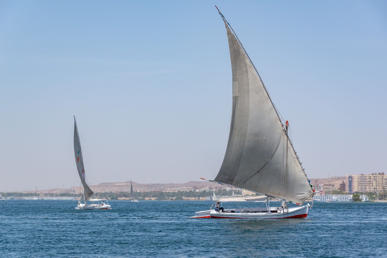 Peaceful scene of sailboats gliding on a clear blue sea under the summer sun.