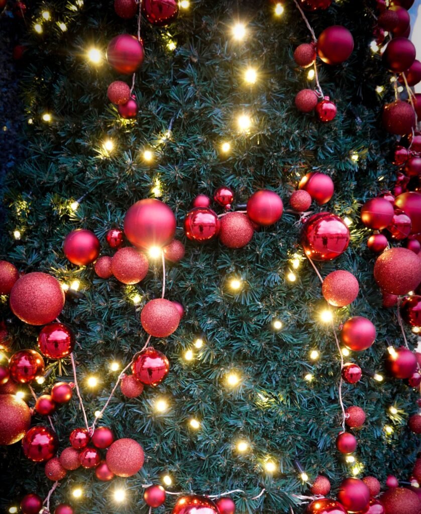 Close-up of a Christmas tree adorned with red ornaments and illuminated by warm lights, creating a festive atmosphere.