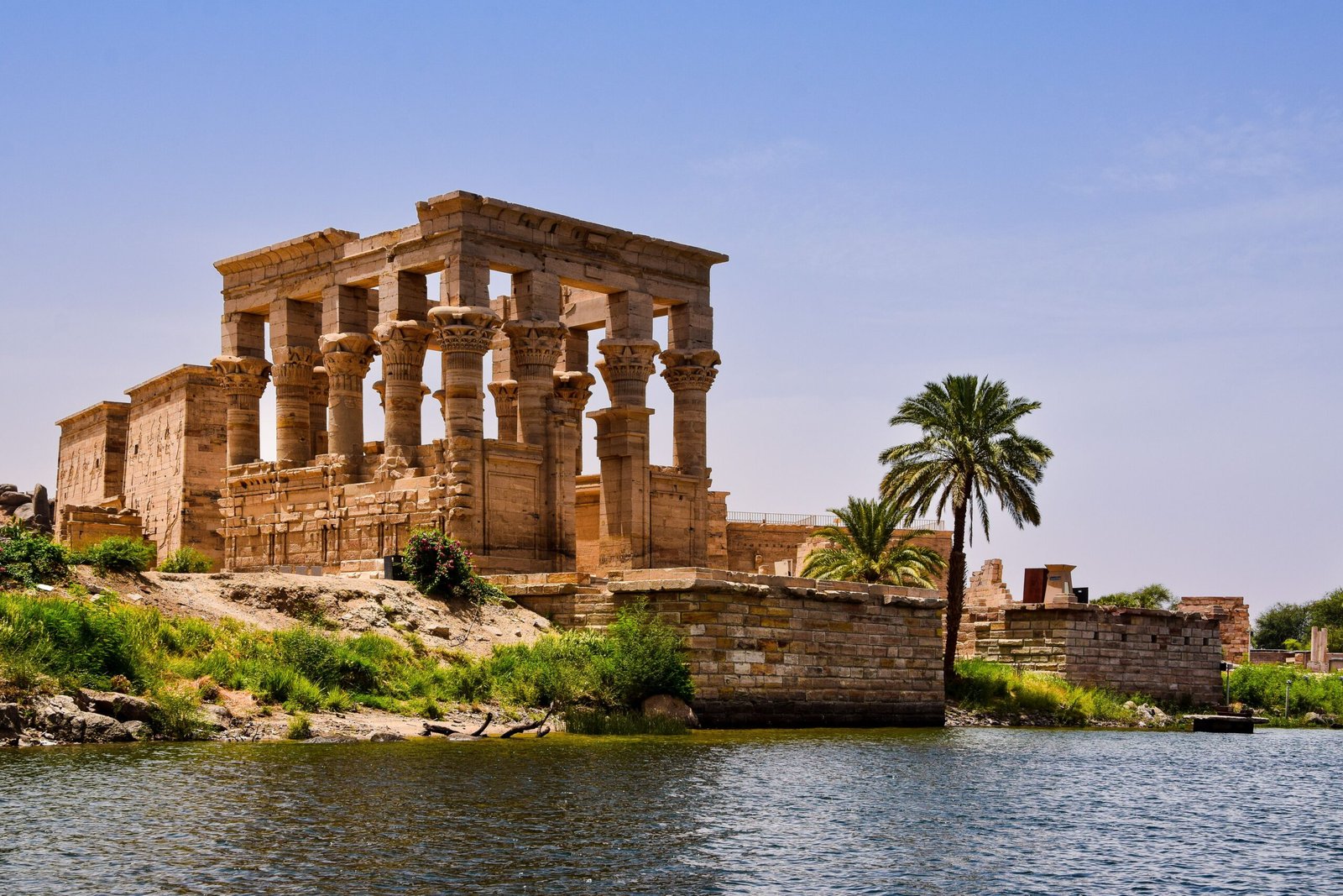 Ancient temple ruins near the Nile River with a palm tree and clear sky.