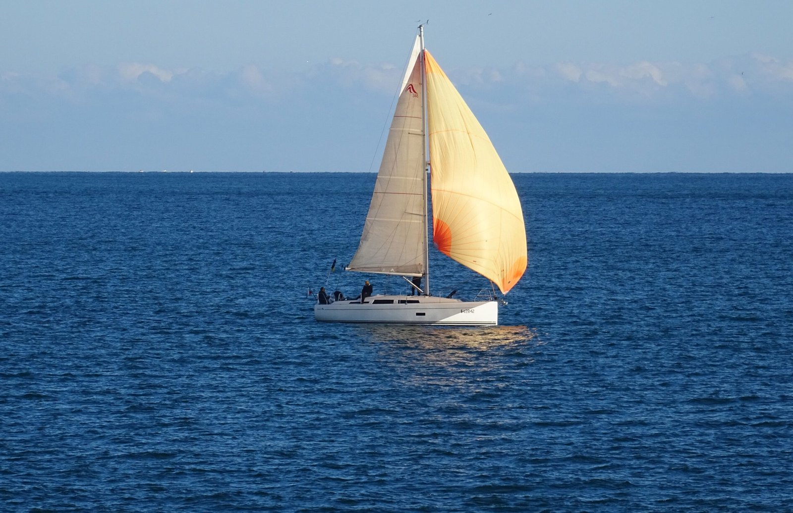 A serene sailboat with beige sails floating on a calm blue ocean during a sunny day.