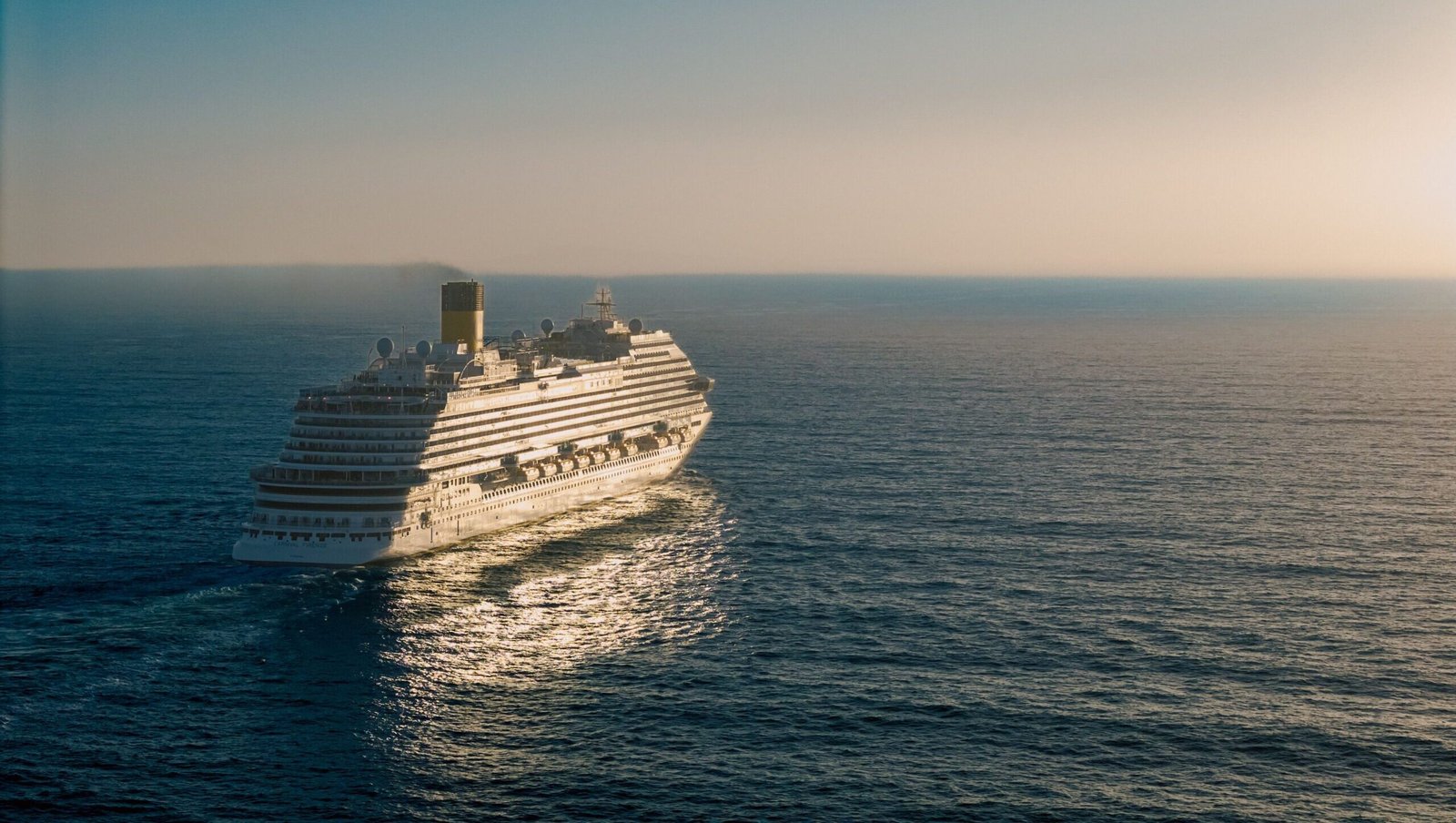 A cruise ship gracefully sails across the ocean at sunset, creating a tranquil scene.