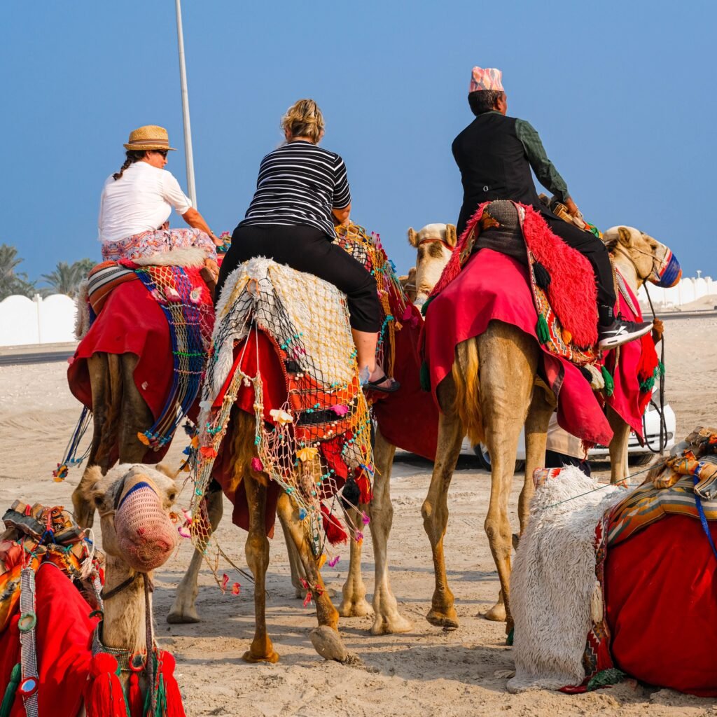 Three tourists on camels adorned with colorful blankets and nets in a desert setting.