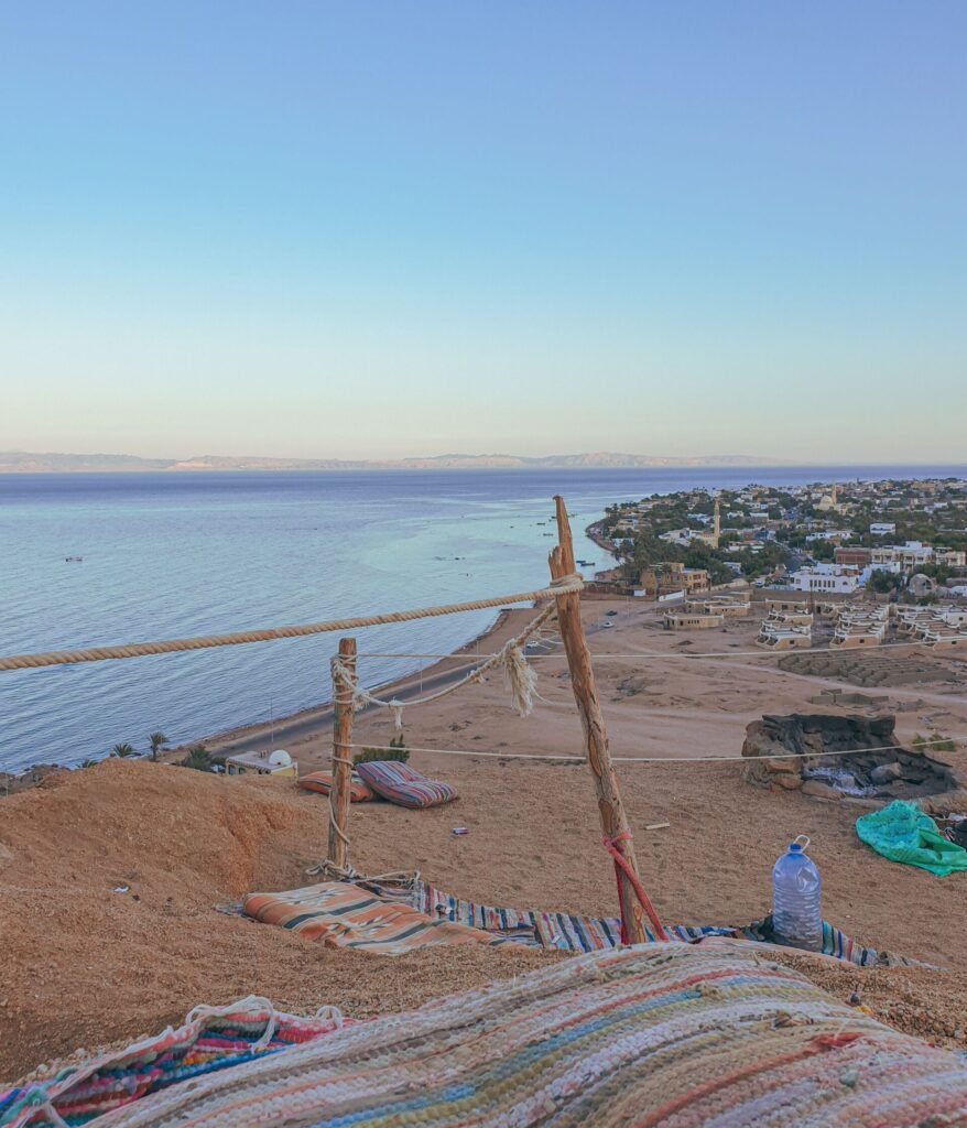Serene view of the rocky Dahab coastline and calm sea under a clear sky during sunset.