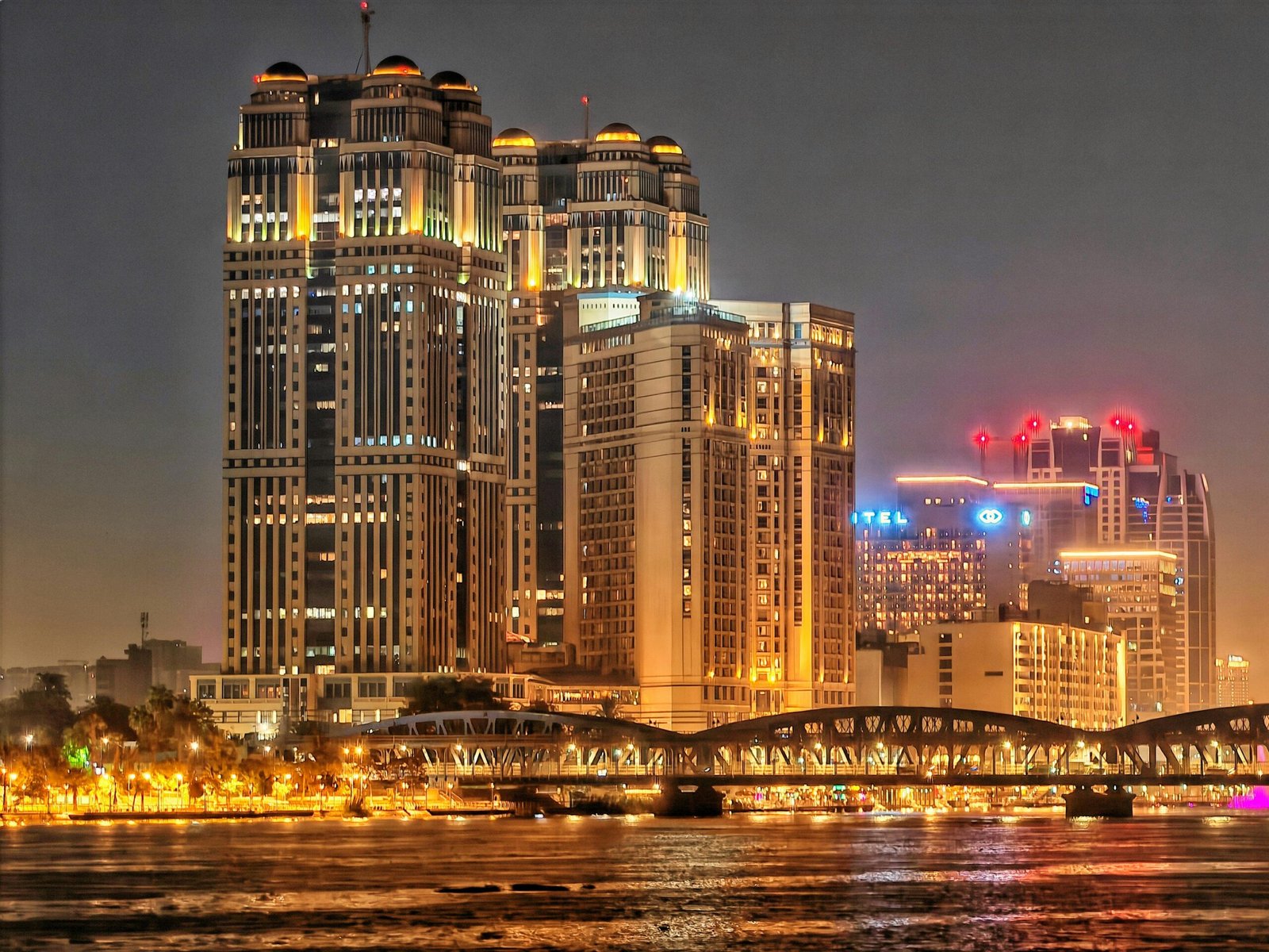 Stunning night view of illuminated skyscrapers and a bridge reflecting on the river.