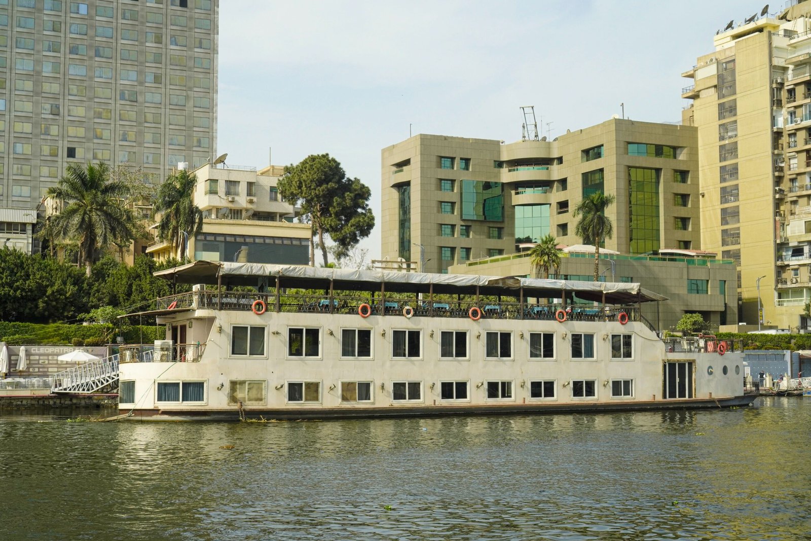 A serene scene of a cruise boat on the Nile River in Cairo, Egypt, with modern buildings in the background.