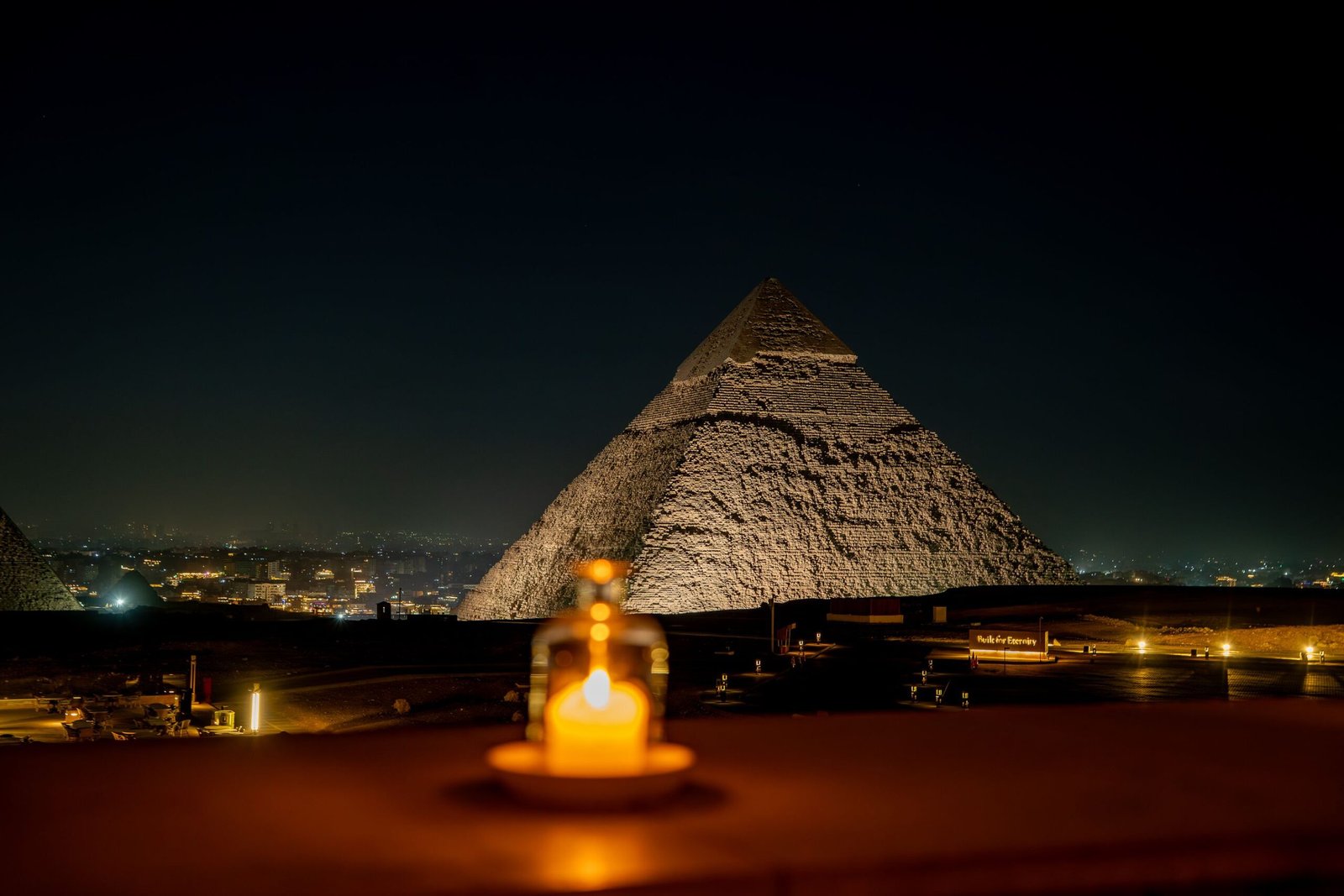 Captivating night view of the Great Pyramid of Giza with a soft glowing candle in the foreground.