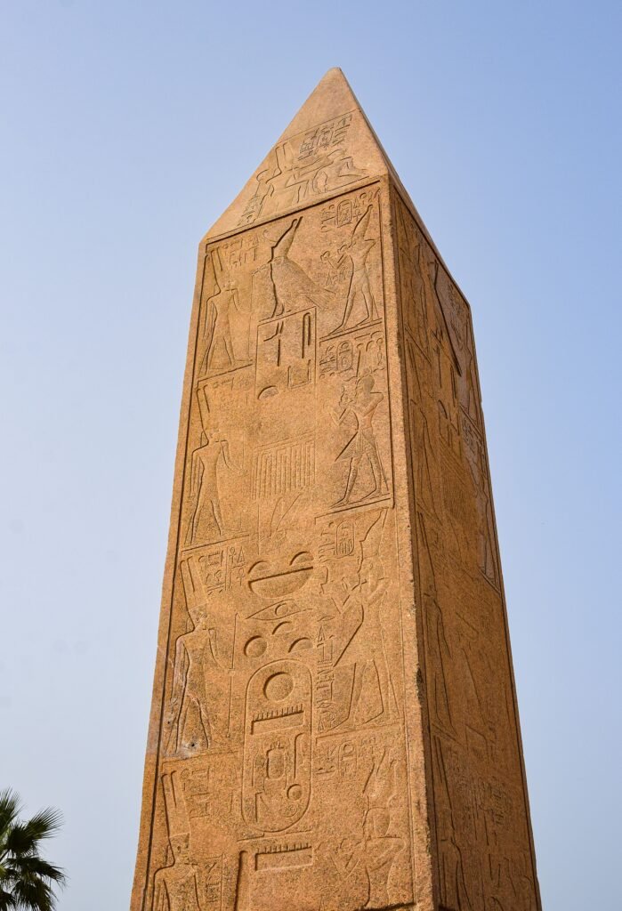 Stone obelisk featuring intricate Egyptian hieroglyphs against a clear blue sky.